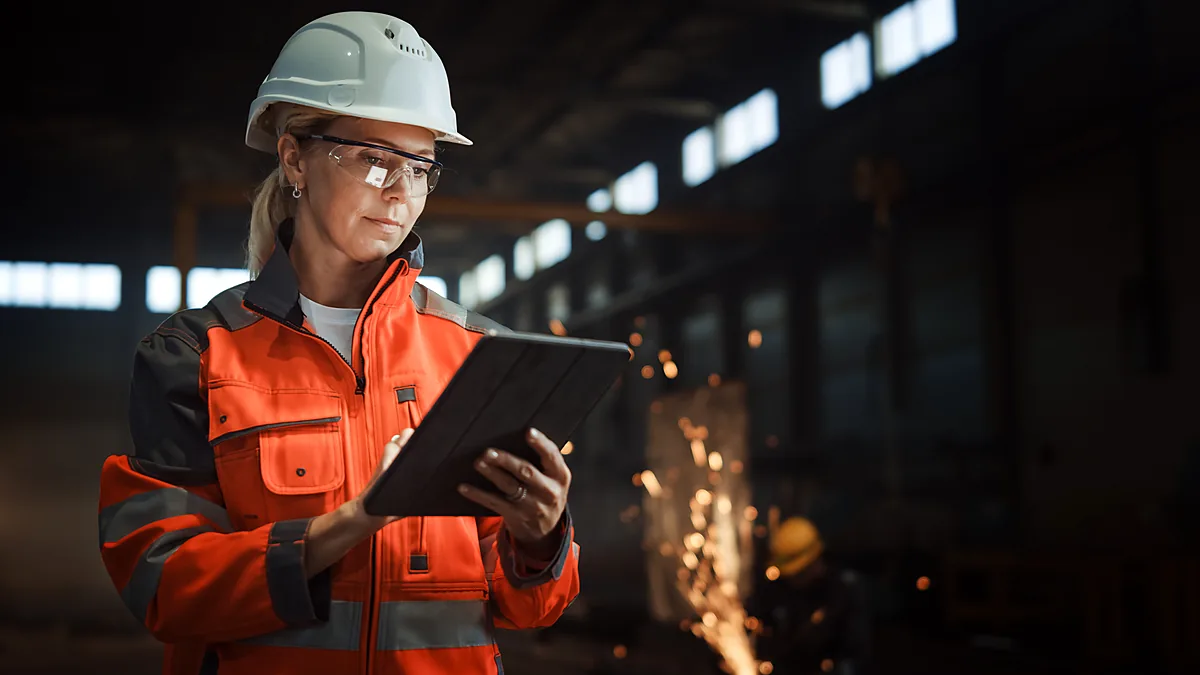 Foundry engineer in safety gear reviewing ERP data on a tablet on the shop floor